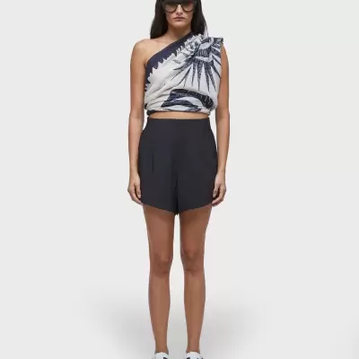 Modelo com top assimétrico branco com padrão preto, calção preto e sapatos brancos, óculos pretos.