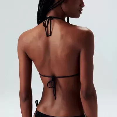 Mulher de costas com biquíni preto de cordões e cabelo trançado