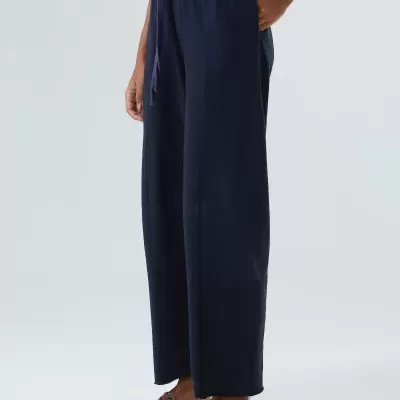 Calças azuis escuras largas com cintura elástica e cordão, usadas com chinelos e camisola preta