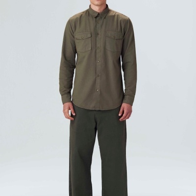 Homem com camisa castanha e calças verdes escuras com chapéu castanho