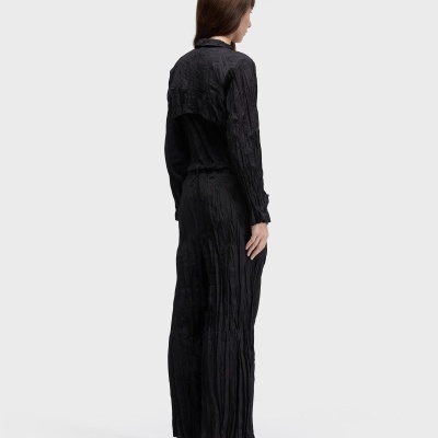 Mulher de costas com vestido preto comprido vincado e sandálias brancas