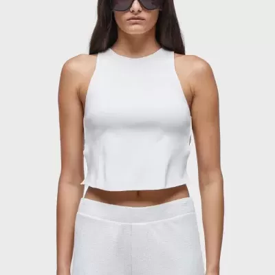 Mulher com top branco cropped e calças brancas, usando óculos escuros pretos.
