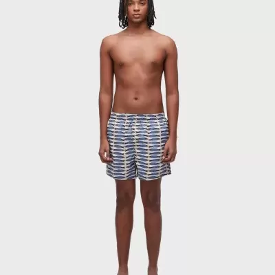 Homem com calções de banho com padrão de peixes e chinelos brancos