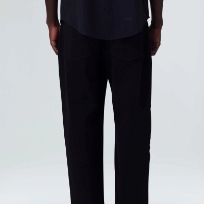 Calças pretas largas vistas de costas com dois bolsos, usadas com camisa e sapatos pretos em fundo claro.