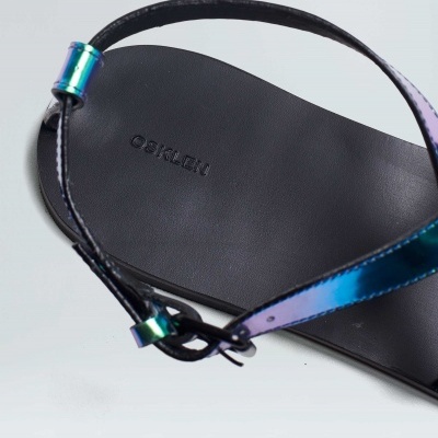 Sandália rasteira preta com tira metalizada azul-roxa.