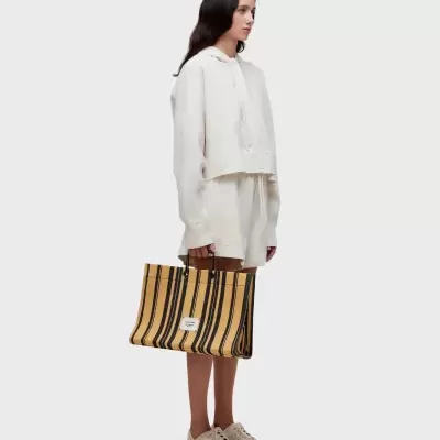 Mulher com roupa casual branca segura mala riscada preta e amarela com etiqueta OWLEN MAISON