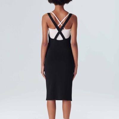 Modelo de espaldas usando vestido preto com alças cruzadas, camisa branca e ténis brancos.