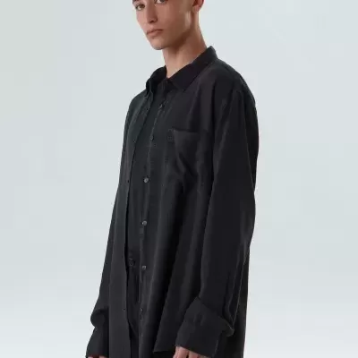 Homem jovem a usar camisa preta oversize com botões