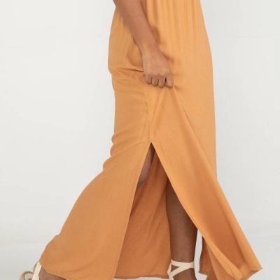 Vestido comprido laranja com fenda lateral e sandálias claras.