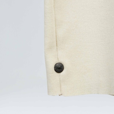 Detalhe da bainha de uma peça de malha bege com botão preto