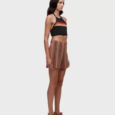 Mulher a usar top cropped com riscas vermelhas e amarelas, saia curta riscada e ténis castanhos com laranja