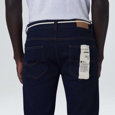 Modelo a usar jeans azul escuro com etiqueta branca no bolso e cinto branco, visto de costas.