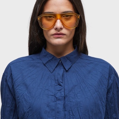 Mulher com óculos de sol amarelos e camisa azul com textura vincada