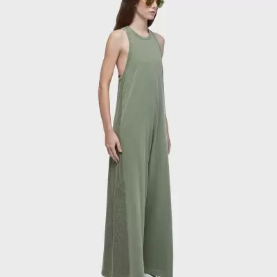 Mulher com macacão verde oliva, óculos amarelos e sapatos brancos