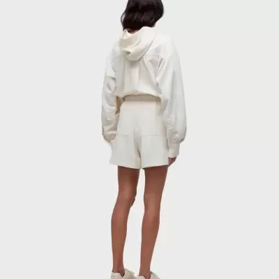 Mulher de costas com casaco com capuz e calções brancos creme e sapatilhas cremadas.