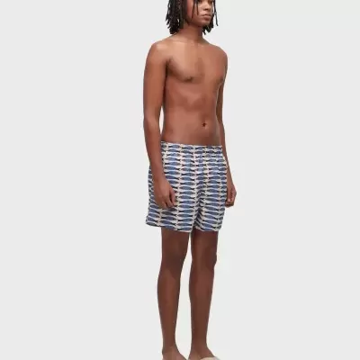 Homem com calção de banho branco com padrão de peixes azuis e castanhos.