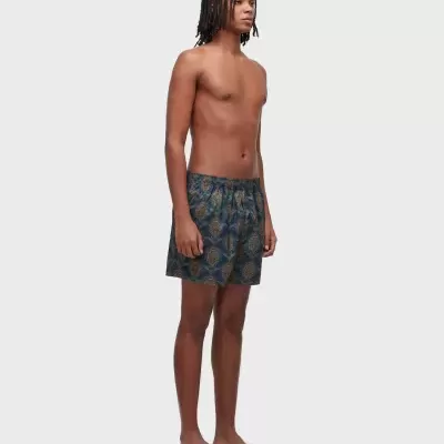 Modelo masculino a usar calções de banho azuis estampados e chinelos brancos