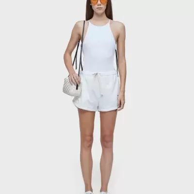 Mulher veste fato de banho branco, calções brancos, ténis brancos, óculos de sol laranja e mala branca