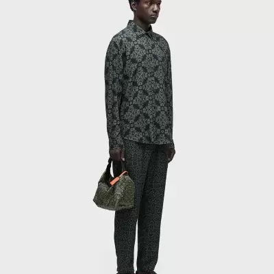 Homem com roupa padrão floral verde e preta segurando bolsa verde texturizada