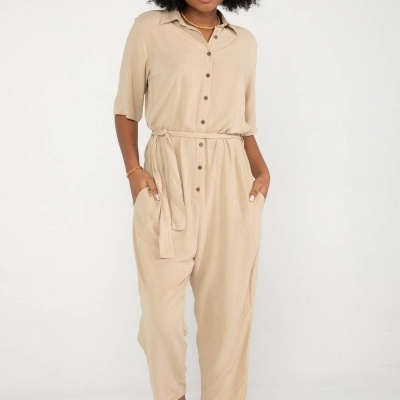 Mulher vestindo macacão bege com botões e cinto, em fundo branco