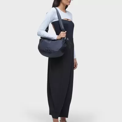 Mochila preta de tecido sintético com alças largas usada por mulher com vestido preto e camiseta branca