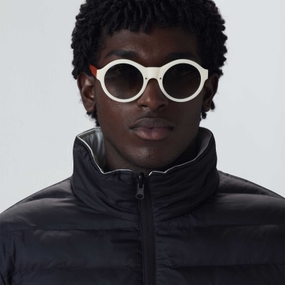 Homem com casaco preto acolchoado e óculos de sol redondos brancos.