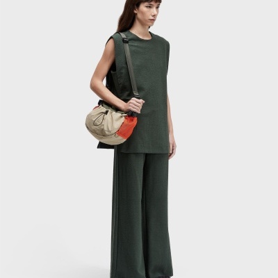 Mulher com conjunto verde escuro e mala tiracolo bege com detalhe laranja, fundo branco.