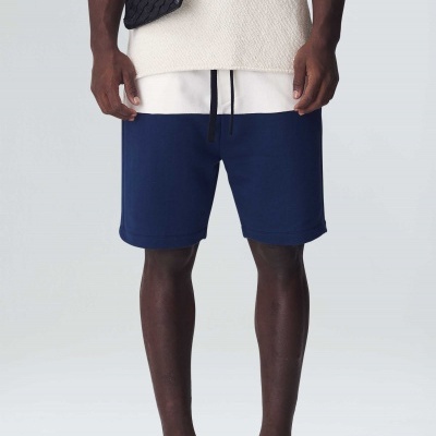 Calções azuis escuros com cordão preto usados por modelo com t-shirt bege e sandálias pretas