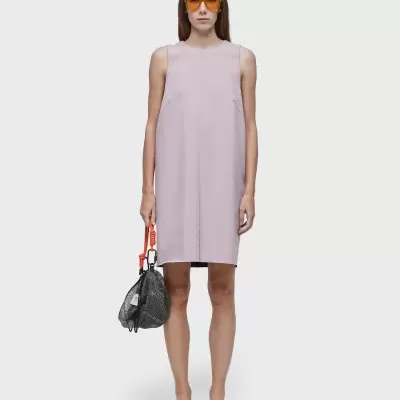 Mulher com vestido lilás claro, óculos laranja, sandálias pretas e mala preta