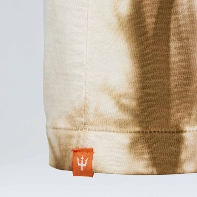 Canto inferior de roupa bege com padrão castanho e etiqueta vermelha com tridente branco.