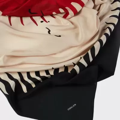 Lenço de tecido com padrão vermelho, bege e preto com a palavra OSKLEN