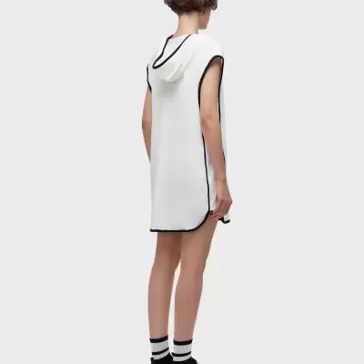 Vestido curto branco com capuz e acabamento preto, meias brancas com riscas pretas e sapatos desportivos brancos e pretos.