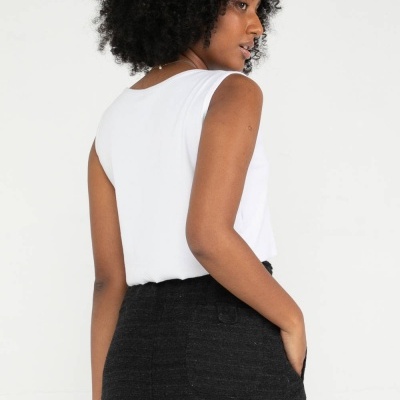 Mulher a usar camisola branca sem mangas e saia preta texturada com bolsos vista de costas