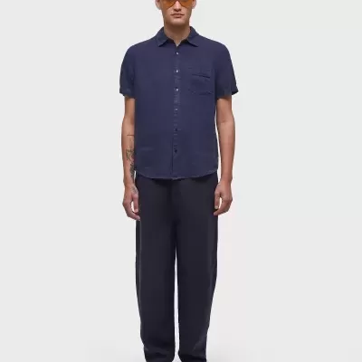 Homem com camisa azul escura, calças largas azuis escuras, sandálias pretas e óculos de sol laranja