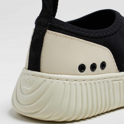 Detalhe traseiro de sapatilha esportiva preta e bege com sola grossa branca e três ilhós negros