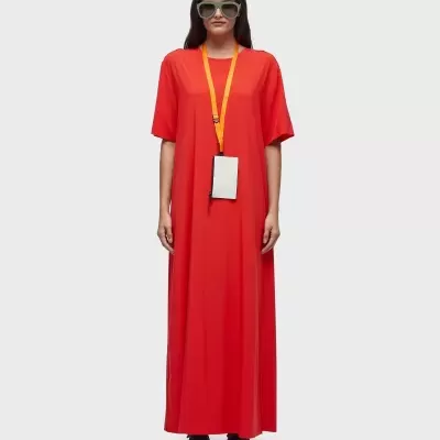 Vestido comprido vermelho com fita laranja ao pescoço usado por modelo de óculos escuros.