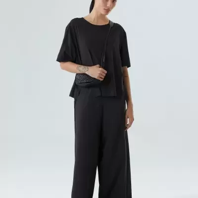 Mulher vestida com roupa preta e bolsa preta num estúdio com fundo branco