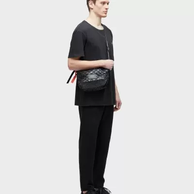 Homem com roupa preta e mala preta com textura e etiqueta branca