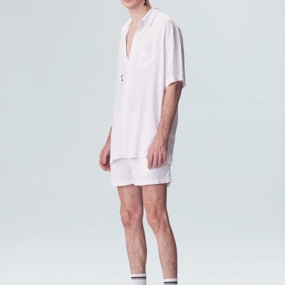 Homem vestido com camisa branca, calções brancos, meias brancas com riscas pretas e ténis brancos