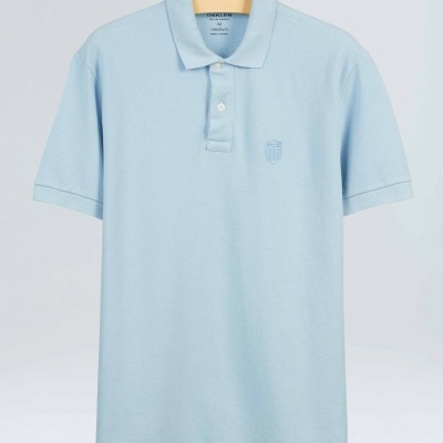 Polo azul claro de algodão com botão e gola, pendurado em cabide de madeira