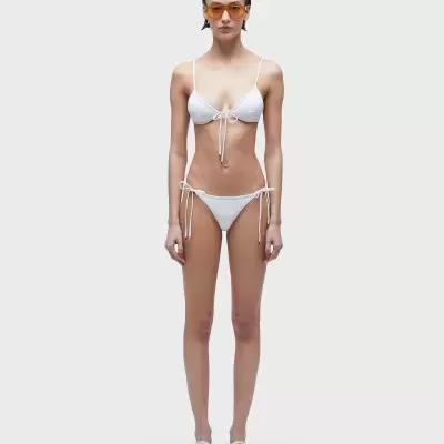 Biquíni branco com amarrações finas usado por modelo com óculos de sol laranja e sandálias brancas