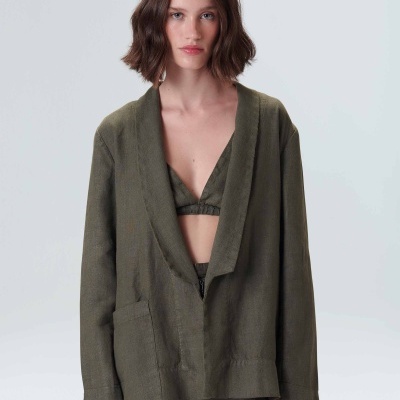 Mulher com blazer verde-oliva, calças e top lingerie, fundo cinzento claro