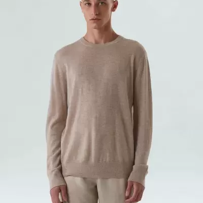 Homem com camisola bege de manga comprida e calças bege claras em fundo branco