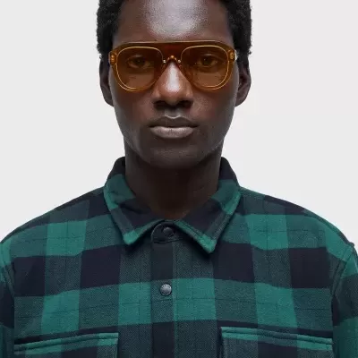 Pessoa com camisa xadrez verde e preta e óculos de armação castanho-âmbar.