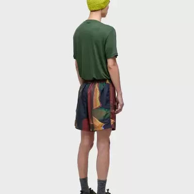 Homem de costas com boné amarelo, t-shirt verde, calções multicoloridos e ténis castanhos.