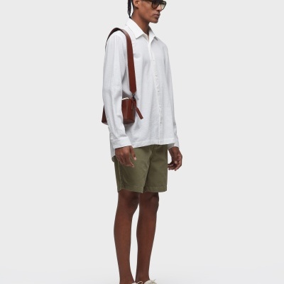 Homem com camisa branca, calções verdes, sapatos brancos e bolsa castanha ao ombro