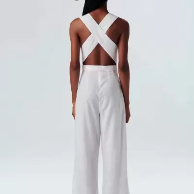 Macacão branco com alças cruzadas e chapéu de palha visto de costas