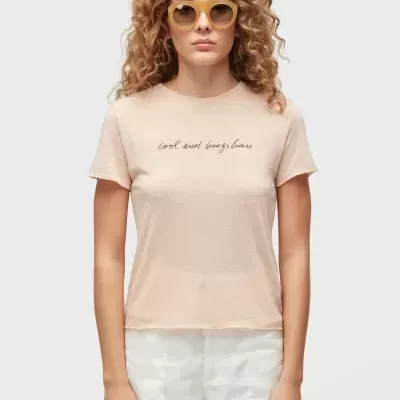 Mulher a usar t-shirt rosa claro com texto e calções brancos, óculos de sol amarelados