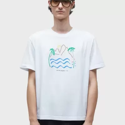 Homem com t-shirt branca estampada, calças pretas e óculos escuros, fundo cinza claro