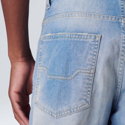 Parte traseira de calças de ganga claras com bolso visível, braço à esquerda e fundo branco